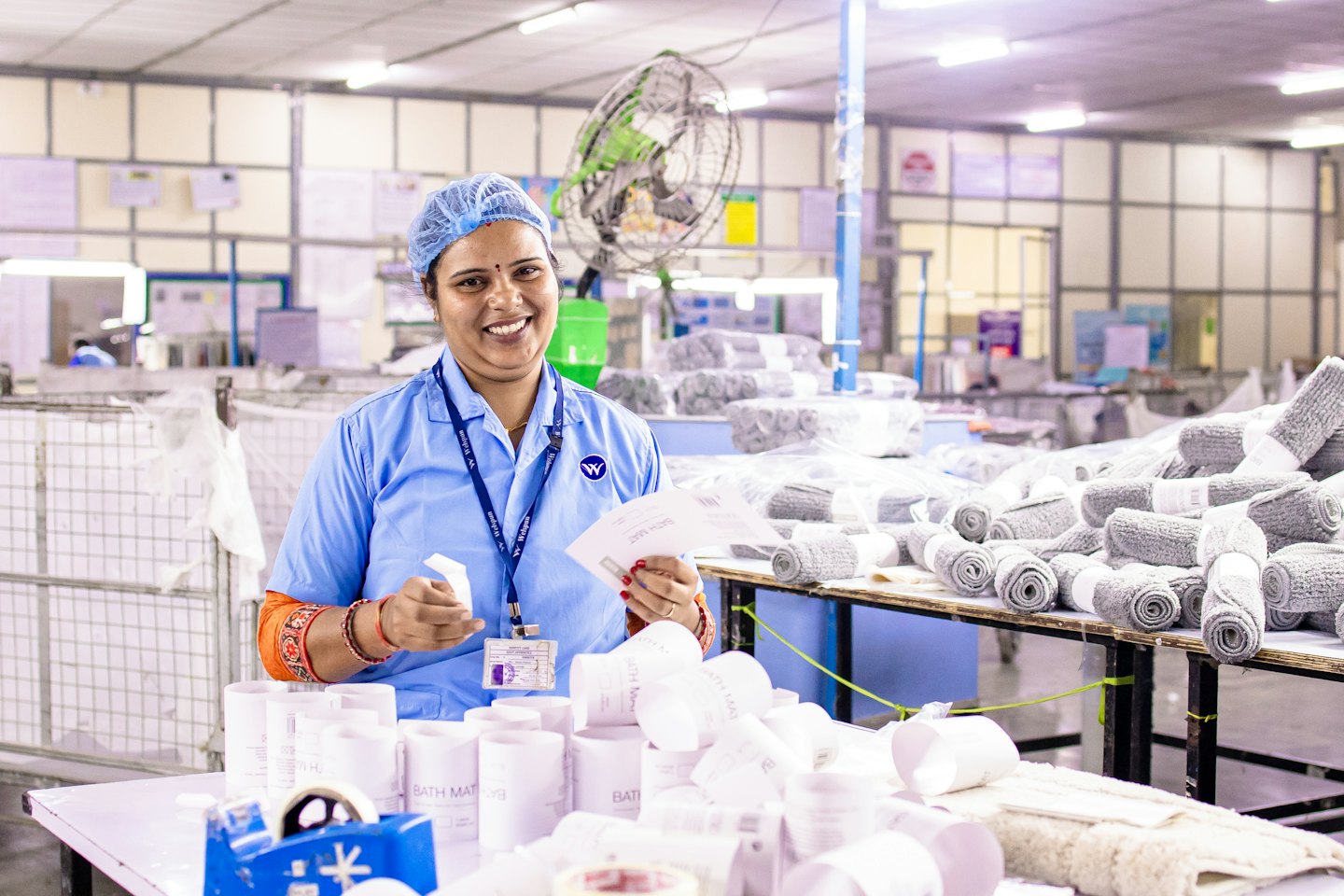Woman in uniform holds product labels at a factory workstation.