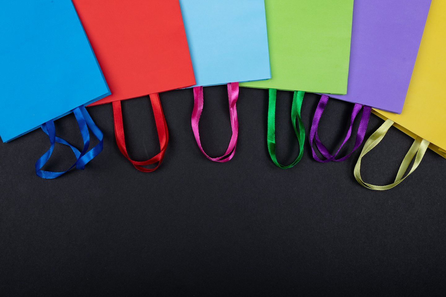 Colorful paper shopping bags with ribbon handles laid out in a row.